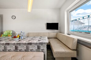 Une pièce moderne avec un canapé, une petite table sur laquelle se trouve un saladier rempli de fruits, une horloge et un téléviseur fixé au mur.