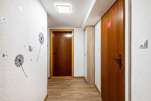 Un pasillo con puertas de madera, paredes blancas con textura y suelo de madera.