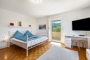 Un dormitorio con cama, mesita de noche, escritorio, silla, televisión y balcón con vistas.