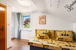 Una habitación con cama, ventana con vistas, puerta y pared con un cuadro enmarcado.
