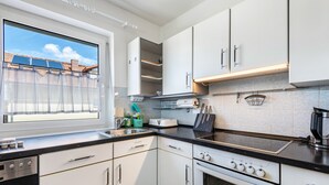 A modern kitchen with white cabinets, a black countertop, a built-in oven, and a window with a view of solar panels. - Holiday Apartment 'Fewo Arber up to 10 Guests, Mountain View' with Balcony & Wi-Fi (Frauenau)