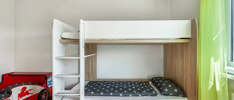 A bunk bed with a pull-out desk, a toy car, and a window with a green curtain.