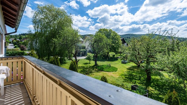A balcony with a view of a green landscape, trees, and a distant house. - Holiday Apartment 'Fewo Arber up to 10 Guests, Mountain View' with Balcony & Wi-Fi (Frauenau)