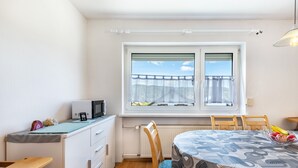 A small, bright room with a window, a table with a patterned tablecloth, a chair, a microwave, and a radiator. - Holiday Apartment 'Fewo Arber up to 10 Guests, Mountain View' with Balcony & Wi-Fi (Frauenau)