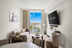 A modern hotel room with a large window, a flat-screen TV, a sofa, a dining table, and a view of the city. - Miami 1BR Condo with Balcony & Leisure Amenities (Miami)