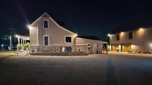 A two-story building with a stone foundation and a sloped roof, featuring a covered porch and a garage. - Labby's Homestead Farmhouse (Hermann)