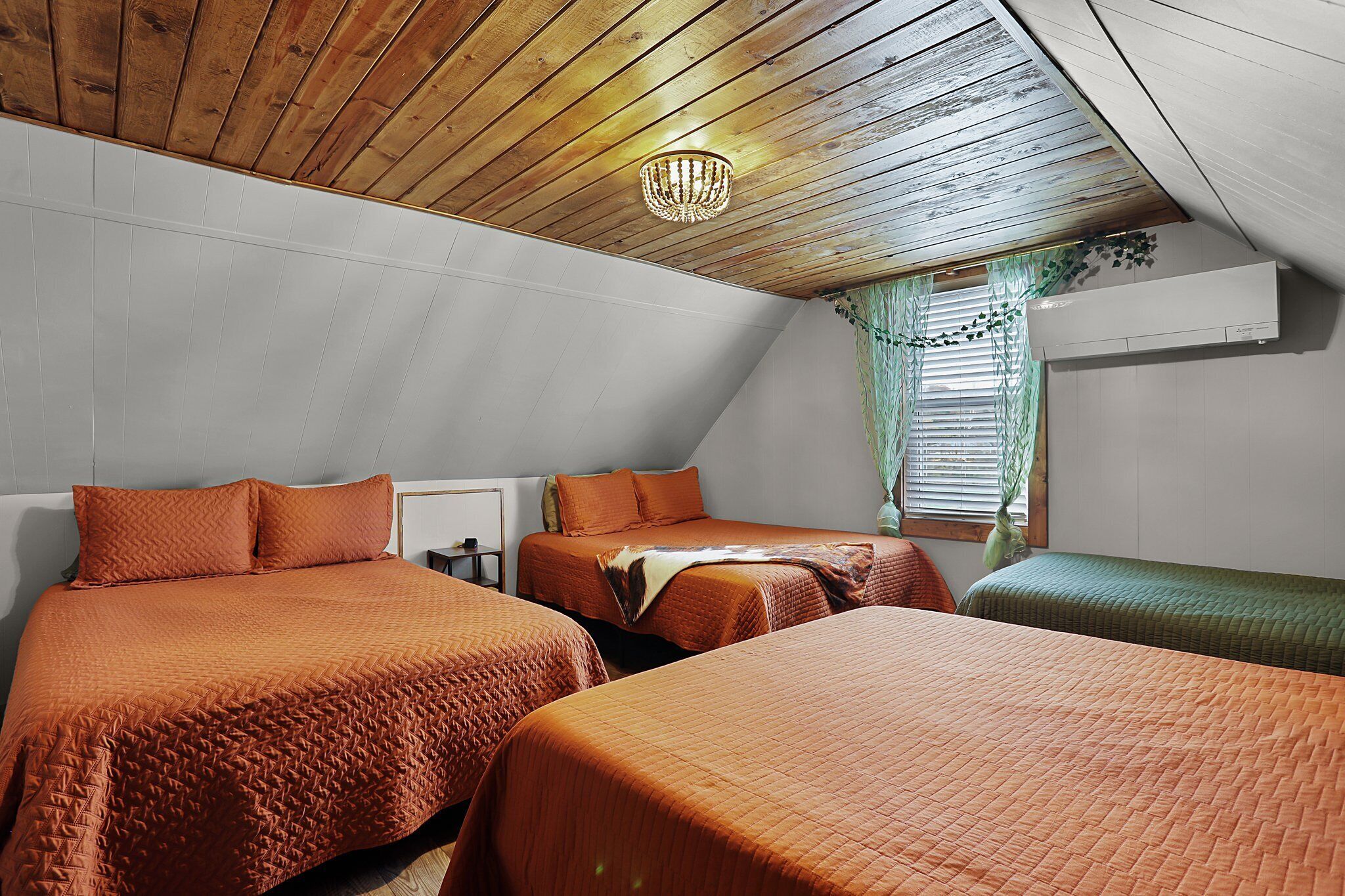 A bedroom with two beds, wooden ceiling, and a window with blinds.
