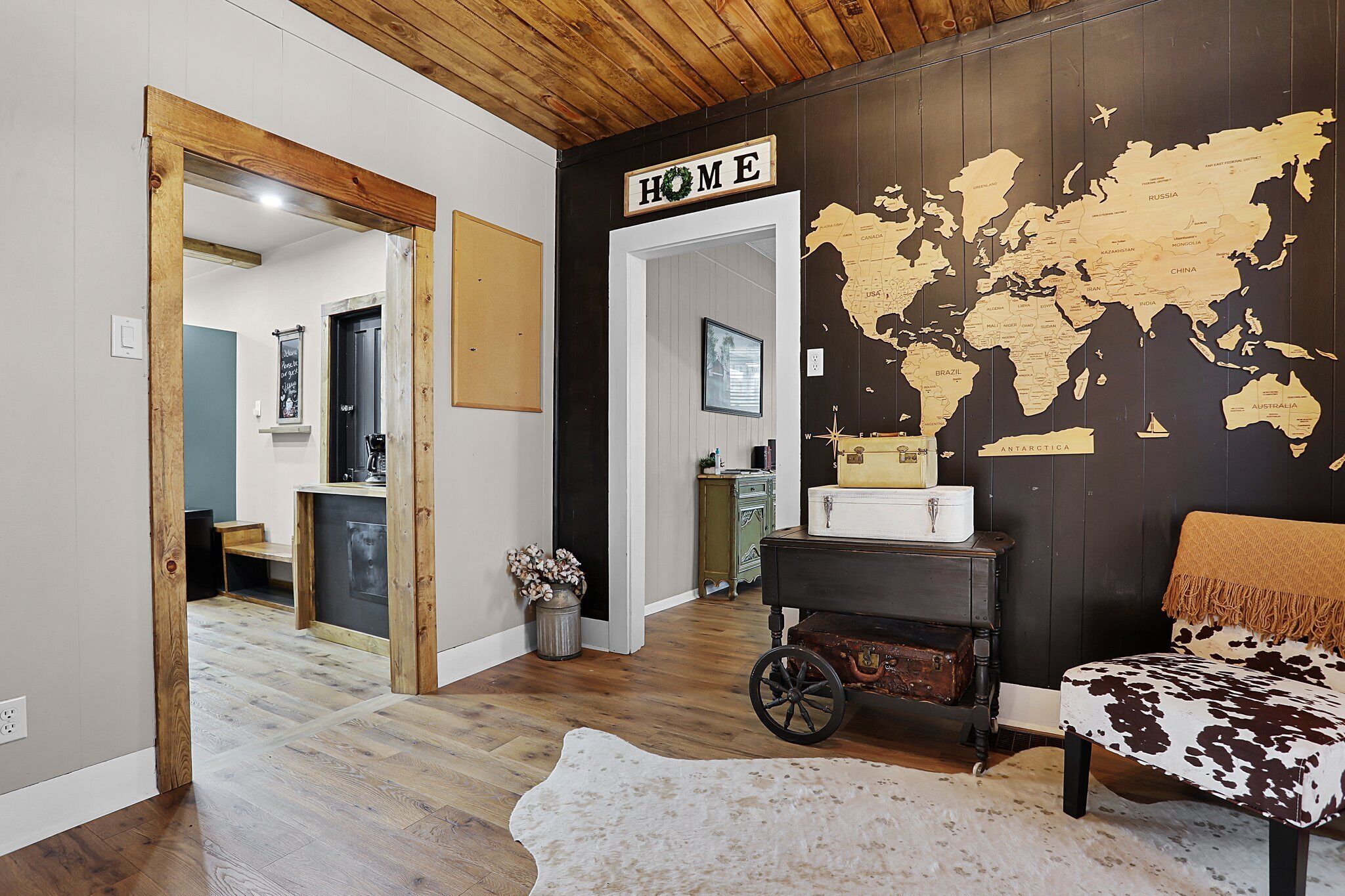 A room with a wooden ceiling, a world map on the wall, a suitcase, and a cowhide rug.
