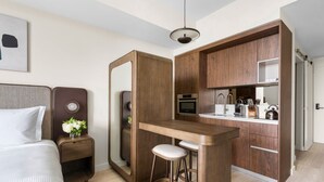 A compact hotel room with a bed, a small bedside table, a mirror, a kitchenette with a microwave, and a bar area with stools. - Ideal Domus Studio a Short Drive to Little Havana (Miami)