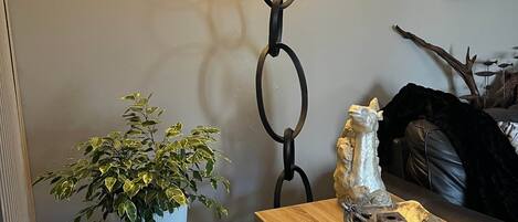 A cozy living room with a potted plant, a table with decorative items, a lamp, and a framed picture on the wall.