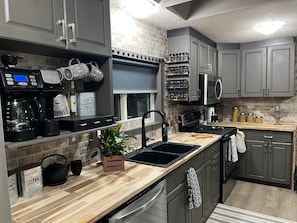 A modern kitchen with grey cabinets, a stainless steel range hood, a coffee maker, and a built-in oven.