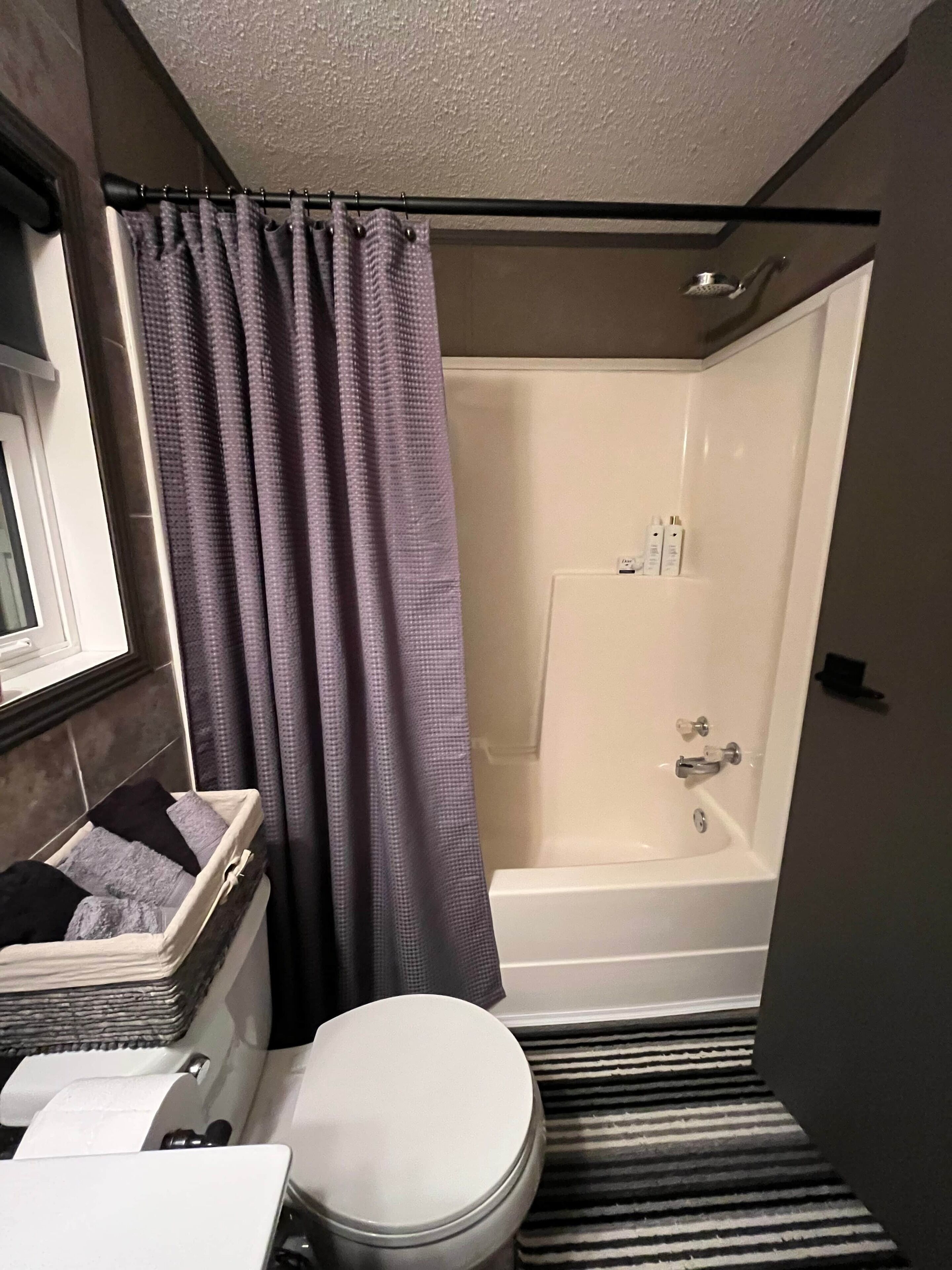 A bathroom with a shower, toilet, and a window.