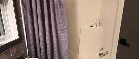A bathroom with a shower, toilet, and a window.