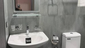Et badeværelse med en hvid vask, et spejl, et toilet og en håndklædestang.