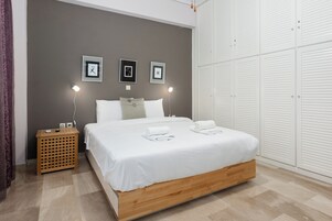 Un dormitorio con cama, mesitas de noche, un armario y cuadros colgados en la pared.