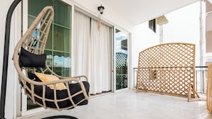 A balcony with a wicker chair, a wooden lattice screen, and a glass door leading to a pool area. - Spacious 144sqm flat near Mount Ymittos (Elliniko-Argyroupoli)