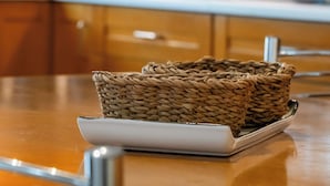 A kitchen with wooden cabinets, a white countertop, and a woven basket on a white plate. - Spacious 144sqm flat near Mount Ymittos (Elliniko-Argyroupoli)