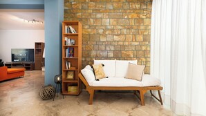 A living room with a stone wall, a sofa, a bookshelf, and a television. - Spacious 144sqm flat near Mount Ymittos (Elliniko-Argyroupoli)