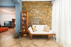 Una sala de estar con pared de piedra, un sofá, una estantería y un televisor.