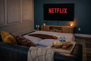 A bedroom with a bed, a TV displaying 'NETFLIX,' a bedside table with a candle, and a tray with snacks. - Ste 717-Free Parking + Skywalk Access + Downtown 2BR City Views (Indianapolis)