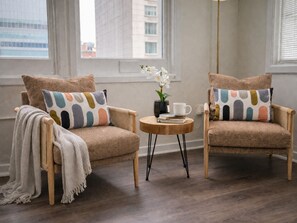 Two armchairs with colorful pillows, a small round table with a book and a cup, and a vase with white flowers. - Ste 717-Free Parking + Skywalk Access + Downtown 2BR City Views (Indianapolis)