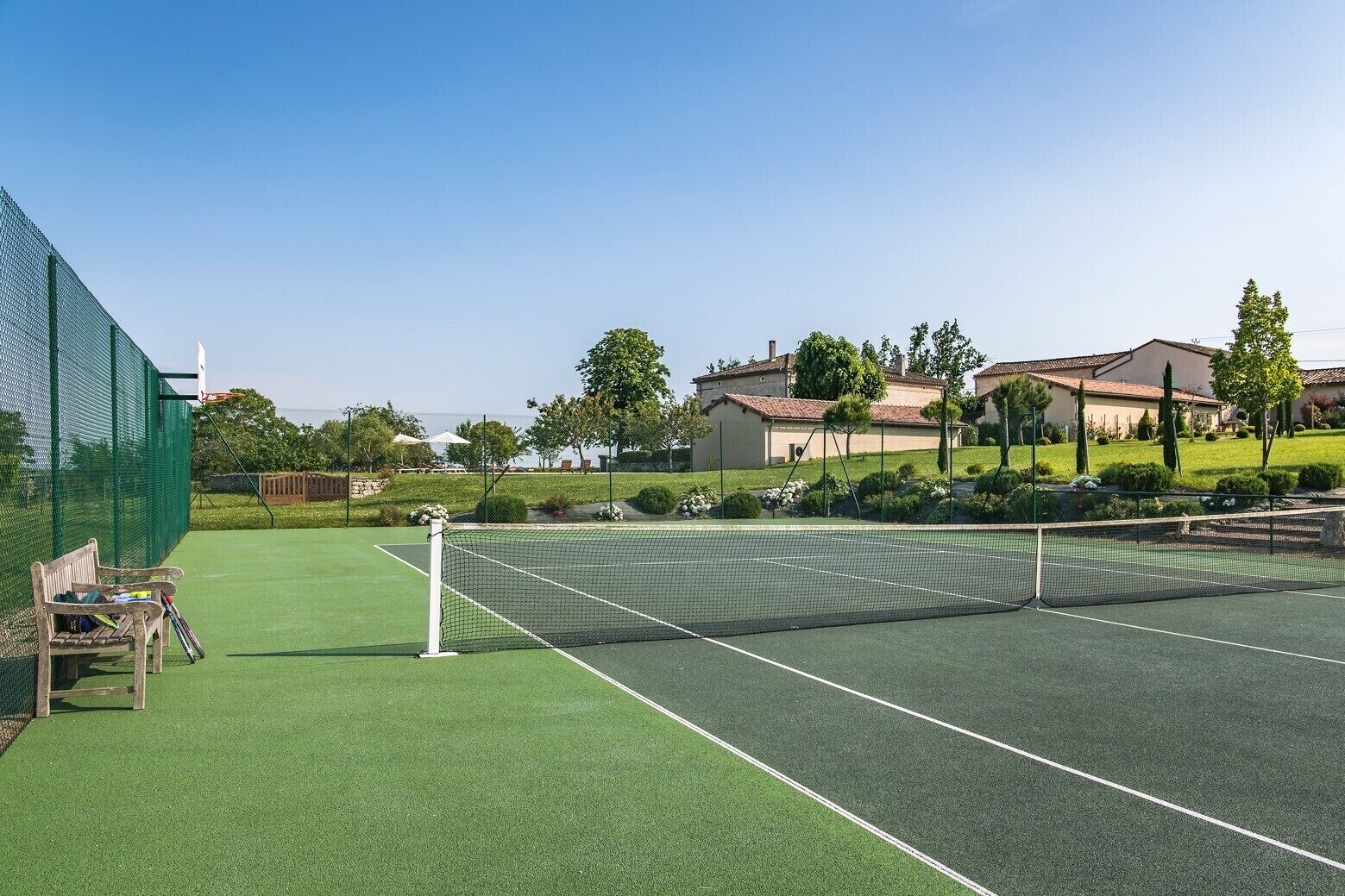 Ein Tennisplatz mit Netz, grünem Kunstrasen und einer hölzernen Bank.