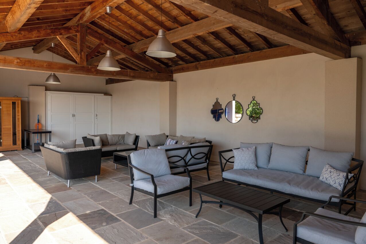 Un espace de vie extérieur doté d’un sol en pierre, d’un plafond en bois et de mobilier comprenant un canapé, des fauteuils et une table.