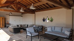 An outdoor living area with stone flooring, a wooden ceiling, and furniture including a sofa, chairs, and a table.