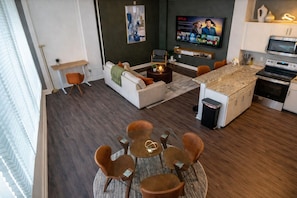 A modern living space with a dining area, kitchen, and a flat-screen TV displaying a movie.