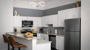 A modern kitchen with white cabinets, stainless steel appliances, a marble countertop, and a unique chandelier. - Ste 421 + Free Parking + Skywalk + Downtown 1BR Near Lucas Oil (Indianapolis)