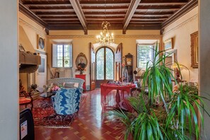 A spacious room with a wooden ceiling, a chandelier, a dining table with a red tablecloth, and a large window. - Suite in a 15th-century villa with private bathroom and pool (Grassina)
