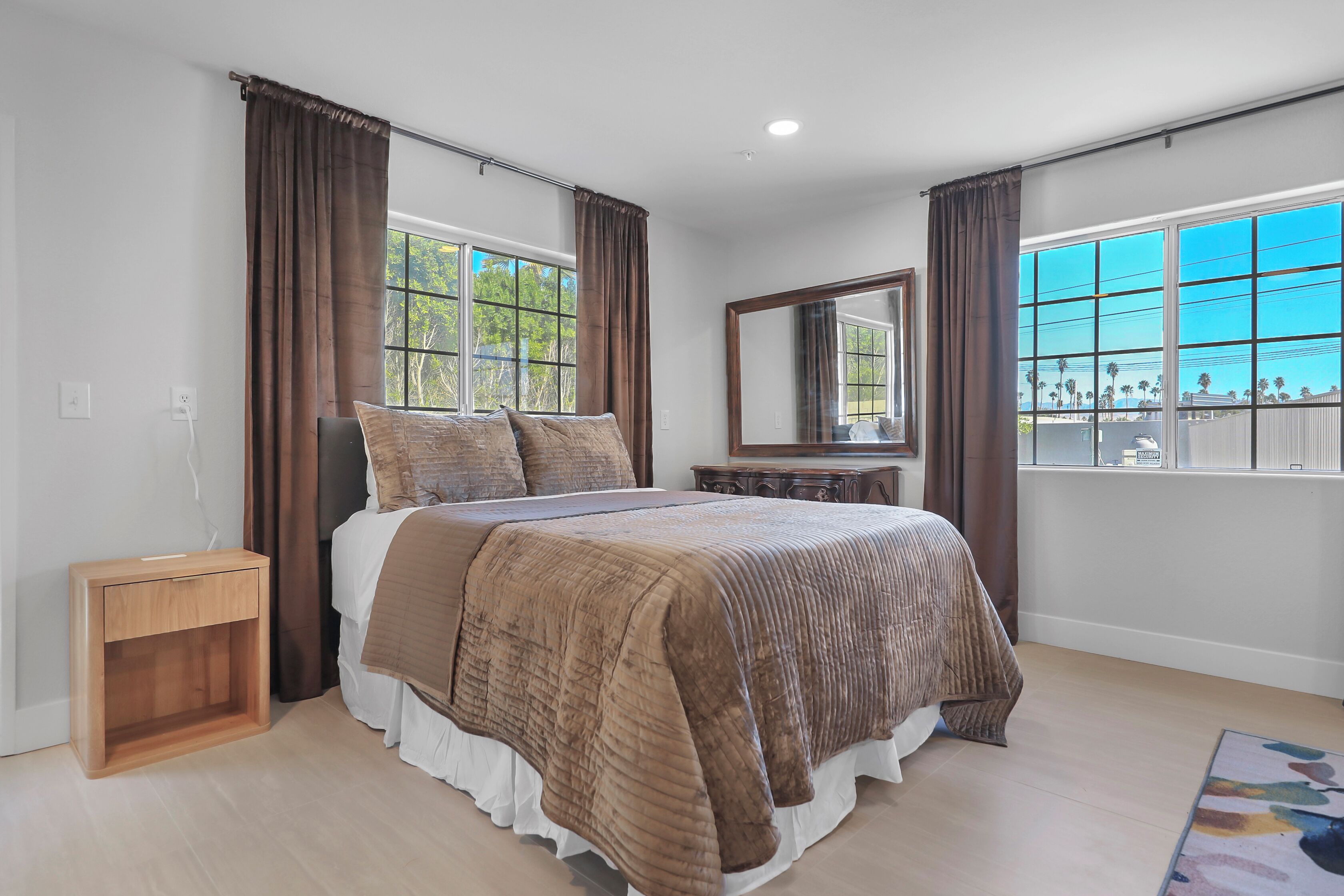 Une chambre à coucher avec un grand lit, une table de chevet, une commode, un miroir et une fenêtre avec des rideaux.