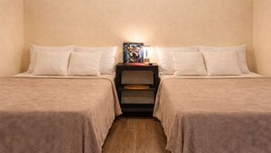 A room with two beds, each with a beige bedspread and white pillows. There is a nightstand between the beds with a lamp and a framed picture. The room has wooden flooring. - Los Cipreses Hotel de Montaña (Los Naranjos)