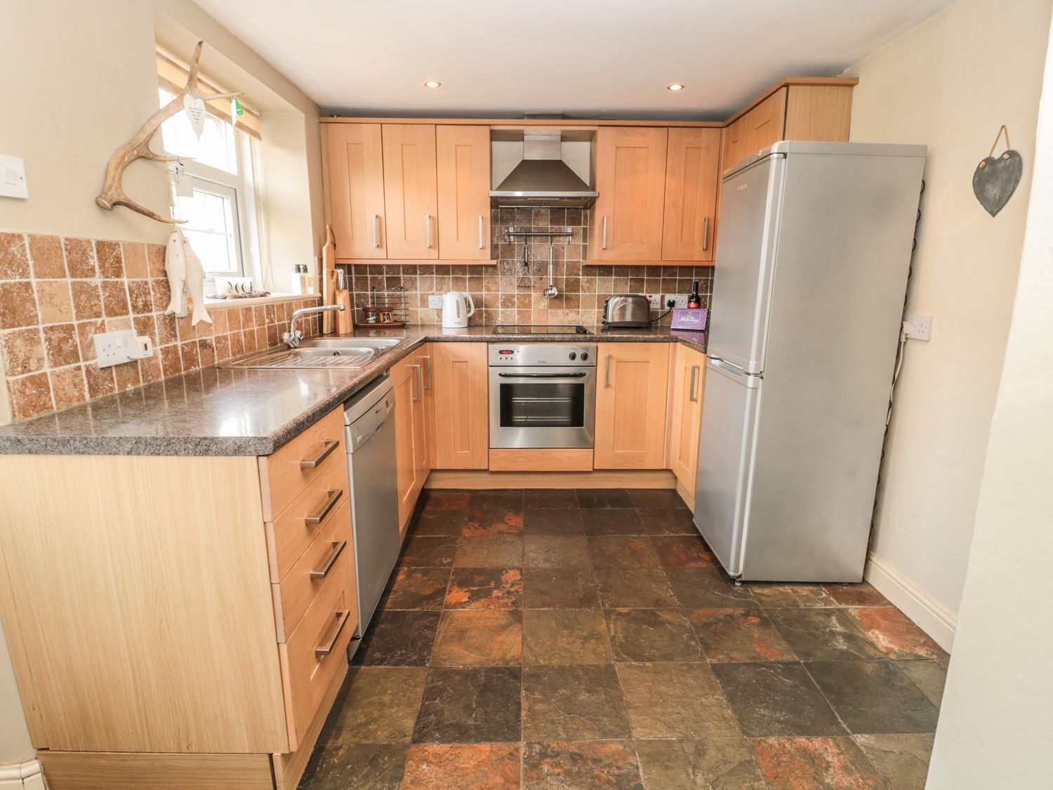 A compact kitchen with wooden cabinets, a stainless steel oven, a refrigerator, and a tiled backsplash.
