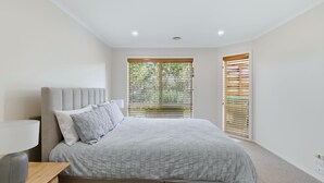 Quarto com cama, mesa de cabeceira, abajur e janela com persianas.