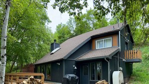 A two-story house with a dark exterior, a wooden deck, and a covered outdoor seating area. - Mountain Cabin in Midway (Midway)