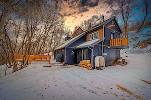 A two-story cabin with a wooden deck and a covered outdoor seating area.
