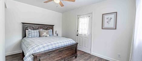 A bedroom with a wooden bed, a ceiling fan, a door with a window, and a framed picture on the wall.