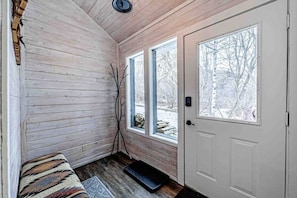 A wooden interior with a bench, two windows, and a door.