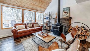 A cozy living room with a leather sofa, a fireplace, and a large window overlooking a deck. - Mountain Cabin in Midway (Midway)