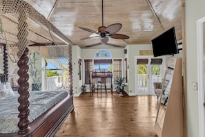 A spacious room with a wooden ceiling, a ceiling fan, a bed with a dark headboard, a dining table with chairs, and a TV mounted on the wall. - Serenity Bay Estate-FL Keys Best Kept Secret! Beautiful, Quiet, Tropical Pardise (Marathon)