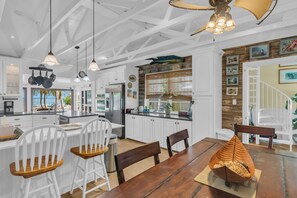 A modern kitchen with white cabinetry, a central island, and a dining area with wooden chairs. - Serenity Bay Estate-FL Keys Best Kept Secret! Beautiful, Quiet, Tropical Pardise (Marathon)