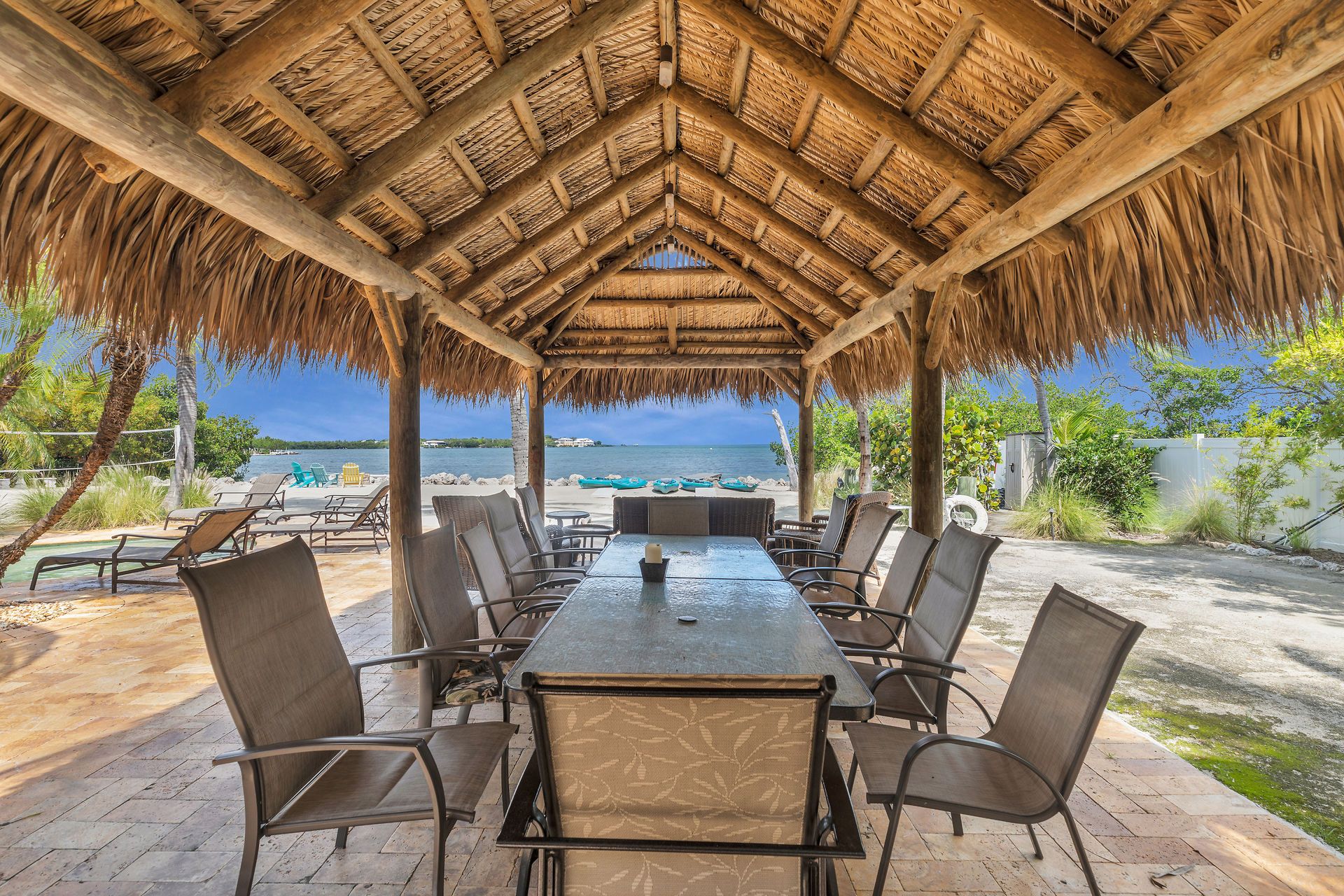 An outdoor dining area with a thatched roof, overlooking a beach and the sea.