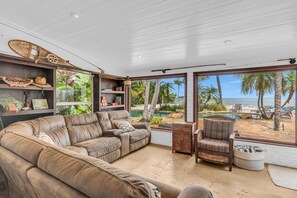 A spacious living room with a large leather sofa, a wicker chair, and a view of a beach and pool. - Serenity Bay Estate-FL Keys Best Kept Secret! Beautiful, Quiet, Tropical Pardise (Marathon)