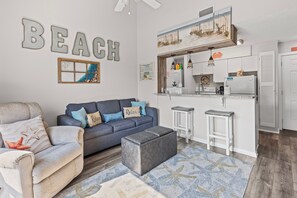 Ein Wohnzimmer mit einer Couch, Hocker und einer Küchenzeile mit Kühlschrank und Arbeitsfläche.