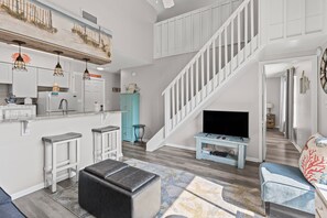 Ein modernes Wohnzimmer mit Küche, Treppe und Fernseher.