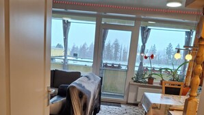 A cozy room with a stone-patterned floor, a covered sofa, a wooden table, and a view of a snowy landscape through large windows. - App 416 Panoramic Hotel Hohegeiß (Braunlage)