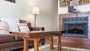 Un salon avec un canapé en cuir marron, une table basse en bois, un lampadaire et une cheminée dotée d’un écran.
