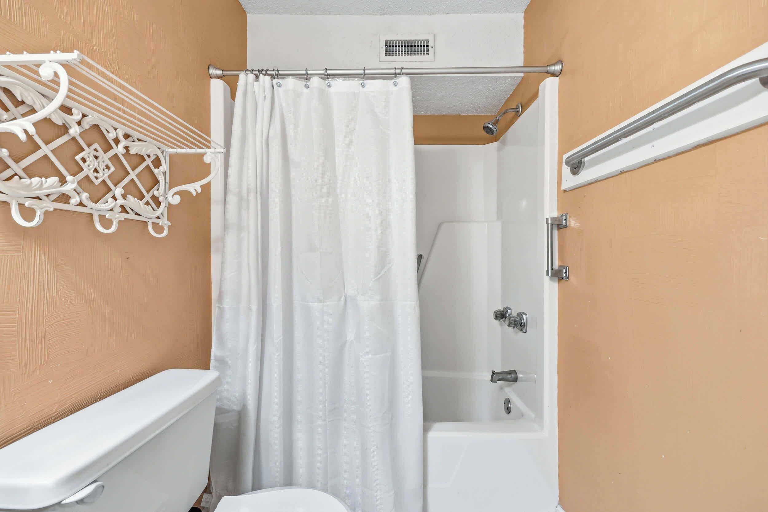 Een badkamer met een wit toilet, een douche met een witte gordijn en een witte handdoekhouder.