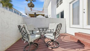 Une terrasse avec deux chaises et une table, un bâtiment blanc et un palmier en arrière-plan.